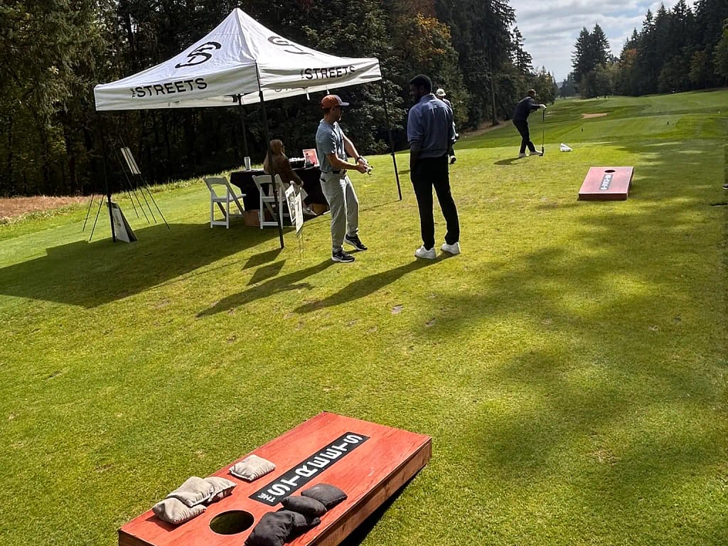 The Streets at Tanasbourne Golf Tournament 2026 tee with cornhole, shade tent and people in the foreground
